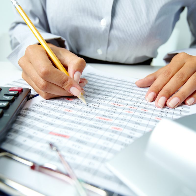 Photo of human hands holding pencil and ticking data in documents